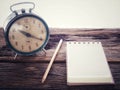 Old wind clock with notebook and pencil on wood table in vintage color scheme Royalty Free Stock Photo