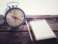 Old wind clock with notebook and pencil on wood table in vintage color scheme Royalty Free Stock Photo