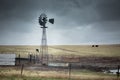 Old windmill in the farmland with cattle in the back on a cloudy day