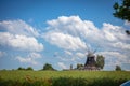 old windmill stands on a canola field in front of a blue sky with white clouds Royalty Free Stock Photo