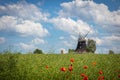 old windmill stands on a canola field in front of a blue sky with white clouds Royalty Free Stock Photo