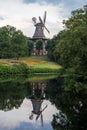 Old windmill in summer park with pond. Windmill with reflection in water in city garden. Royalty Free Stock Photo