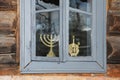 An old window with broken glass in an old wooden house. On the window there are symbols of the Jewish people - candlesticks of the