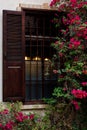 Old window with brown wooden window shutters and warm light inside the building and beautiful flowers of pink bougenvilla outside Royalty Free Stock Photo