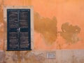 Old window with green painted closed wooden shutters on an orange Mediterranean ocher colored orange cracked peeling flaking wa Royalty Free Stock Photo