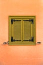 Old window with green wooden shutters on a vivid orange wall, closeup background. Royalty Free Stock Photo