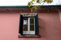 Old window on pink wall with green shutters and yellow leaves. Royalty Free Stock Photo
