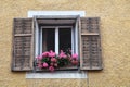 old window in a stone wall with wooden shutters and geraniums on the window sill Royalty Free Stock Photo