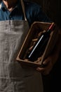 Old winemaker holding a wooden box with bottle of red wine