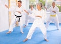 Old woman attendee of karate classes practicing kata standing in row with others Royalty Free Stock Photo