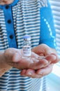 Old woman in blue t-shirt holding vaccine vial glass bottle for vaccination against COVID-19 coronavirus pandemic in her hands. Royalty Free Stock Photo