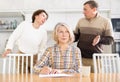 Old woman compiling heritage document while middle-aged man and woman competing in the kitchen Royalty Free Stock Photo