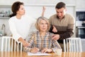 Old woman compiling heritage document while middle-aged man and woman competing in the kitchen Royalty Free Stock Photo