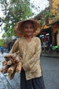 Old woman with face showing lines of hard life wearing a tatty conical hat and carrying load of bundles of cane