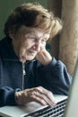 An old woman, granny, is study typing on a laptop at her home.