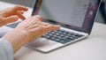 Old woman hands type on black keyboard of grey laptop on white table with bright light reflections in office at work Royalty Free Stock Photo