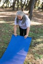 Old woman holding yoga mat and preparing to practice yoga or meditation outdoors on park. Happy mature woman with Royalty Free Stock Photo