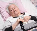 Old woman lying in bed and holding dollar cash Royalty Free Stock Photo