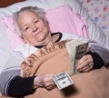 Old woman lying in bed and holding dollar cash money Royalty Free Stock Photo