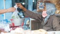 An old woman with a mask on her face is selling her wares at the traditional Market