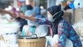 An old woman with a mask on her face is selling her wares at the traditional Market