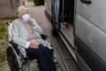 An old woman in a medical mask with a wheelchair, getting a disabled person into the car. Royalty Free Stock Photo