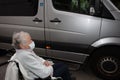 An old woman in a medical mask with a wheelchair, getting a disabled person into the car. Royalty Free Stock Photo