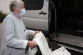 An old woman in a medical mask with a wheelchair, getting a disabled person into the car. Royalty Free Stock Photo