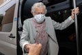 An old woman in a medical mask with a wheelchair, getting a disabled person into the car. Royalty Free Stock Photo