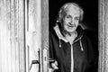 An old woman peeks out from behind door of house. Black and white photo. Royalty Free Stock Photo