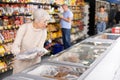 Old woman purchaser choosing frozen fish in big supermarket