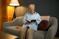 Old woman reading book sitting on sofa Royalty Free Stock Photo