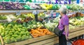 The old woman is selecting fruits from stall in the supermarket. Old consumer with healthy and fresh vegetables