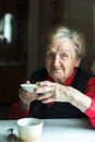 An old woman sits drinking tea, a portrait of grandmother in her home.