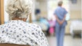 An old woman sits in a hospital corridor waiting to see a doctor.