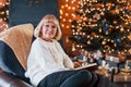 Old woman sitting on the chair with book in festive New year room with christmas decorations Royalty Free Stock Photo