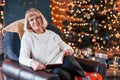 Old woman sitting on the chair with book in festive New year room with christmas decorations Royalty Free Stock Photo