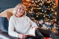 Old woman sitting on the chair with book in festive New year room with christmas decorations Royalty Free Stock Photo