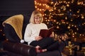 Old woman sitting on the chair with book in festive New year room with christmas decorations Royalty Free Stock Photo