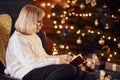 Old woman sitting on the chair with book in festive New year room with christmas decorations Royalty Free Stock Photo