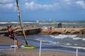 Old Woman Sitting on the Rocks near Coastline Looks at Young Surfer on the Beach