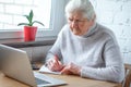 An old woman is sitting at the table in front of laptop Royalty Free Stock Photo