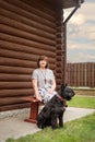 An elderly woman is sitting on a village bench with a black schnauzer near a wooden house in the countryside