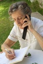An old woman is speaking on mobile phone and taking some notes in her agenda Royalty Free Stock Photo