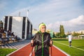 Old woman in sportswear practicing nordic walking outdoors on rubber treadmill in stadium. Older female walk by scandinavian walk