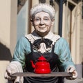 Old woman statue holding a red tea kettle Royalty Free Stock Photo