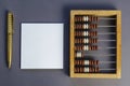 Old wooden abacus, square blank white paper gold-colored pen on gray background Royalty Free Stock Photo