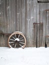 Old wooden barn wall with an old wooden cartwheel in snow Royalty Free Stock Photo