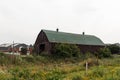 Old wooden barn - weathered texture - green metal roof - surrounded by wild grass and plants - cloudy sky backdrop Royalty Free Stock Photo