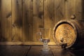 Old wooden barrel with a tap and an empty glass cup in the twilight on a wooden background Royalty Free Stock Photo